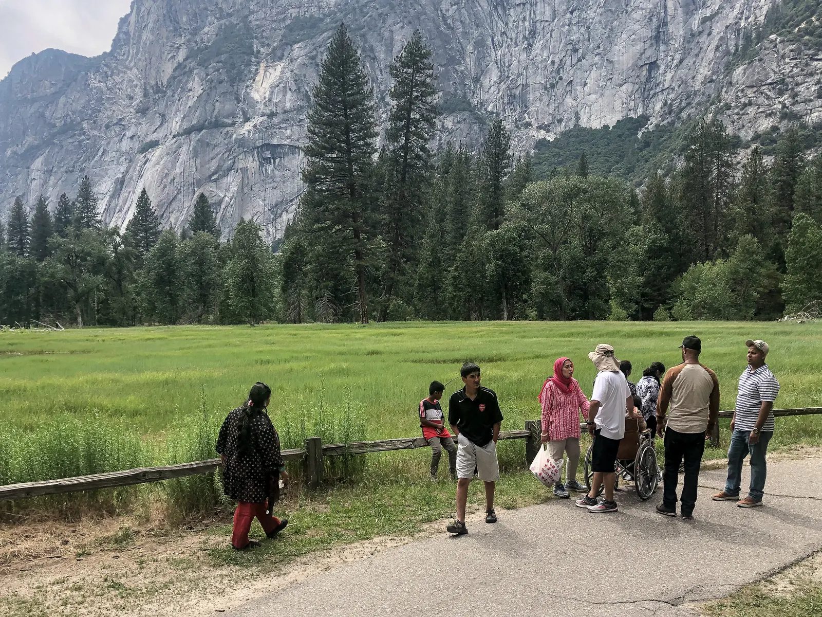 遊客沿著草甸邊的步道行走，背景是樹林與高聳山壁。