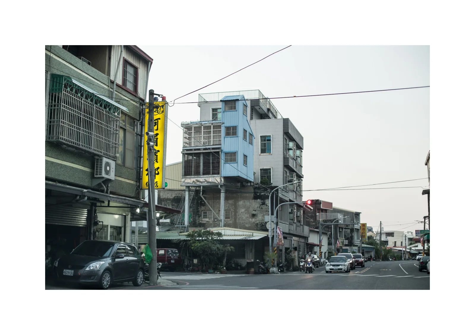 小冊子《1》第 7 頁：街道兩側的樓房、招牌與車輛，中間一棟樓房帶有大型格柵。