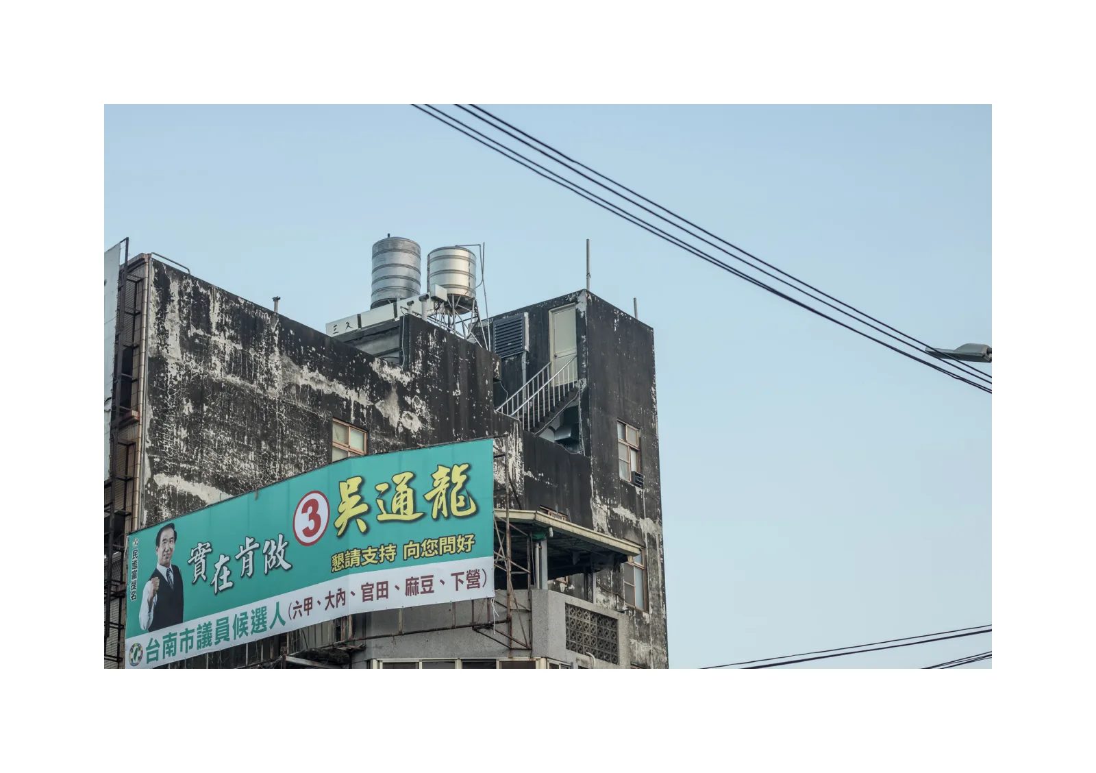 小冊子《B》第 5 頁：斑駁建築外牆掛著綠色廣告看板，屋頂可見兩個水塔。